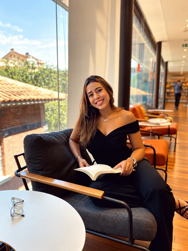 Amanda Terra lendo em uma poltrona junto a uma janela ampla, com a cidade ao fundo