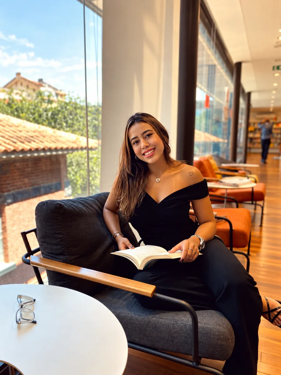 Amanda Terra lendo em uma poltrona junto a uma janela ampla, com a cidade ao fundo