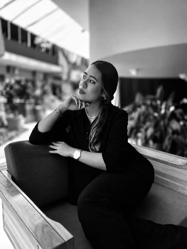 Amanda Terra sentada em um sofá, em fotografia preto e branco, olhando para o lado com a mão no queixo
