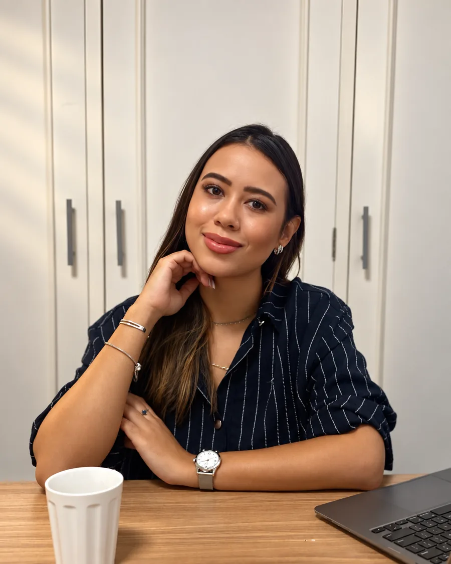 Amanda Terra sorrindo, sentada à mesa com uma xícara e o notebook, em conversa próxima